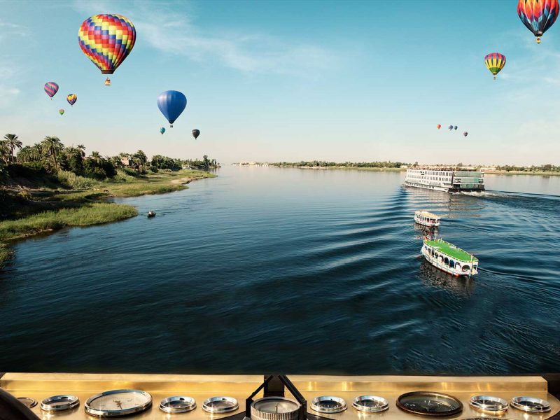 Media capturing hot air balloons flying over the Nile River.