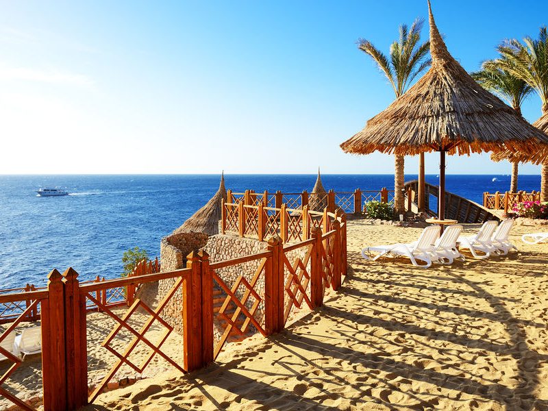 A picturesque beach in Sharm El-Sheikh adorned with comfortable lounge chairs and charming thatched umbrellas, perfect for a relaxing seaside experience.